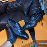 Black leather shoes on a Louis Vuitton box with a black leather couch and boxes in the background.